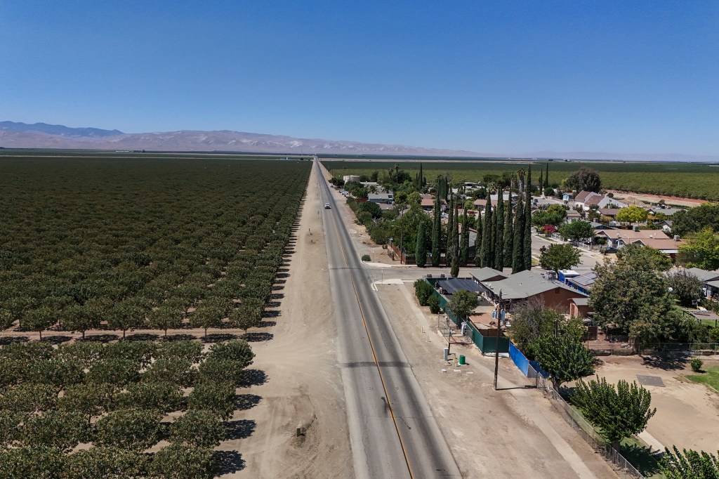 An aerial view of the main road going through the farm community of Cantua Creek with rows of orchards surrounding the town.