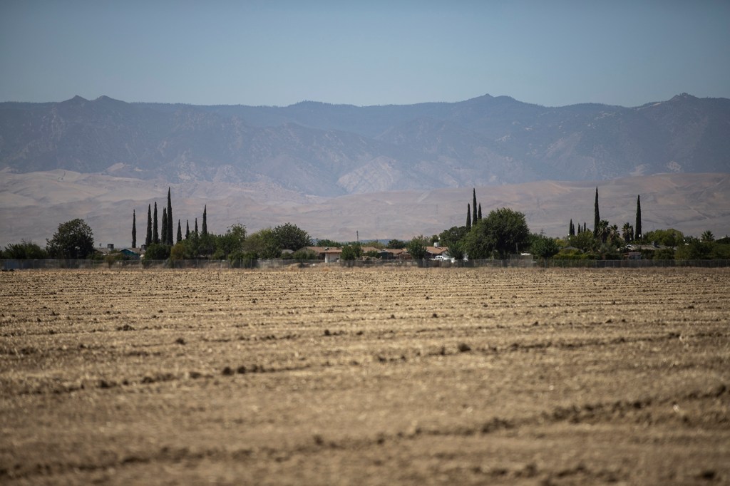 A view of the town of Cantua Creek across from an agricultural field with a view of a mountain range in the distance.