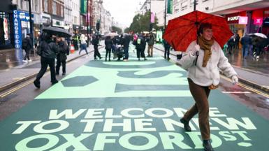 A woman walking down the newly pedestrianised Oxford Street holding a red umbrella