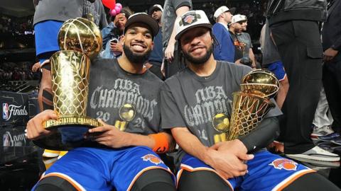 Karl-Anthony Towns and Jalen Brunson celebrate winning the NBA Championship holding trophies