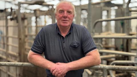 George McMaster dairy farmer. George has grey hair and is wearing a blue top.
