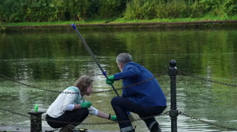 A man and a woman collecting water samples from a river