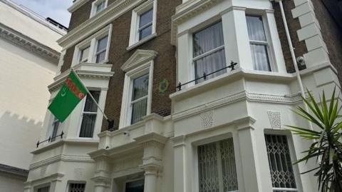 A house with a Turkmenistan flag and national emblem attached to its outside wall