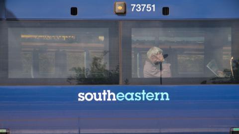 The side of a blue Southeastern Railways carriage. Behind one of the two windows, commuters sit waiting for the train to continue its journey. - stock photo