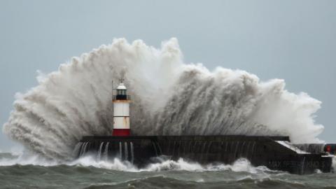 A large wave crashes on a harbour arm.
