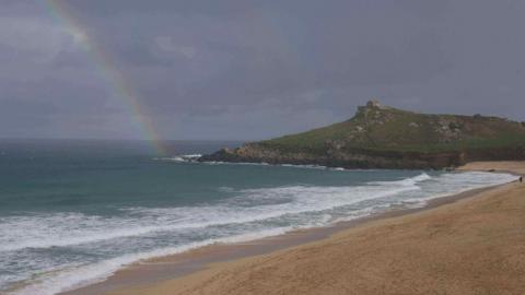 A general view of Porthmeor beach in St Ives in St Ives on a stormy day. There is a rainbow.