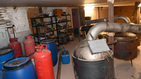 A basement containing at least three gas red canisters, large plastic tubs and several containers connected to metal tubing.