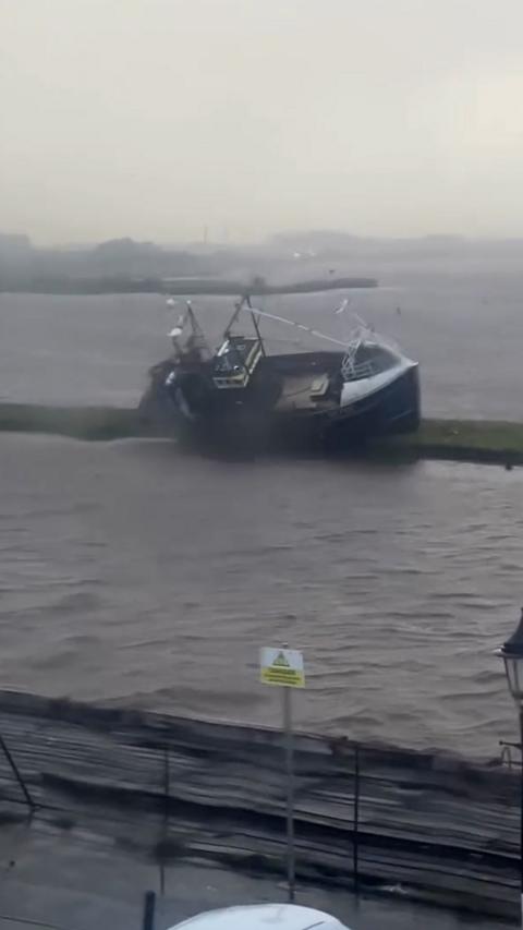 A wet grey scene showing high tides and a tilted boat at a harbour.