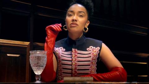 Leigh-Anne Pinnock wearing a military-style top and red long gloves, sitting at the round table
