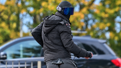 A man on a bike wearing a balaclava and large protective glasses so his face is unrecognisable.
