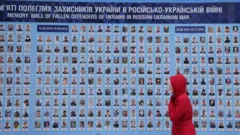 کییف، اوکراین - ۲۱ ژانویه: زنی در حال عبور از کنار «دیوار یادبود» در شهر کییف اوکراین (۲۱ ژانویه ۲۰۲۲)؛ دیواری که تصاویر، اسامی، و تاریخ تولد و وفات حدود ۴۵۰۰ سرباز حرفهای و داوطلب را در خود جای داده است؛ کسانی که در جریان درگیریهای جاری در منطقه دونباس، در راه دفاع از اوکراین جان باختهاند.