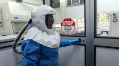 Umukozi wo muri laboratwari wambaye imyenda yo kumurinda, mu gihe yitegura kwinjira muri laboratwari ipimirwamo Ebola, mu kigo cya Uganda cy'ubushakashatsi kuri virusi, kiri i Entebbe, muri Uganda.