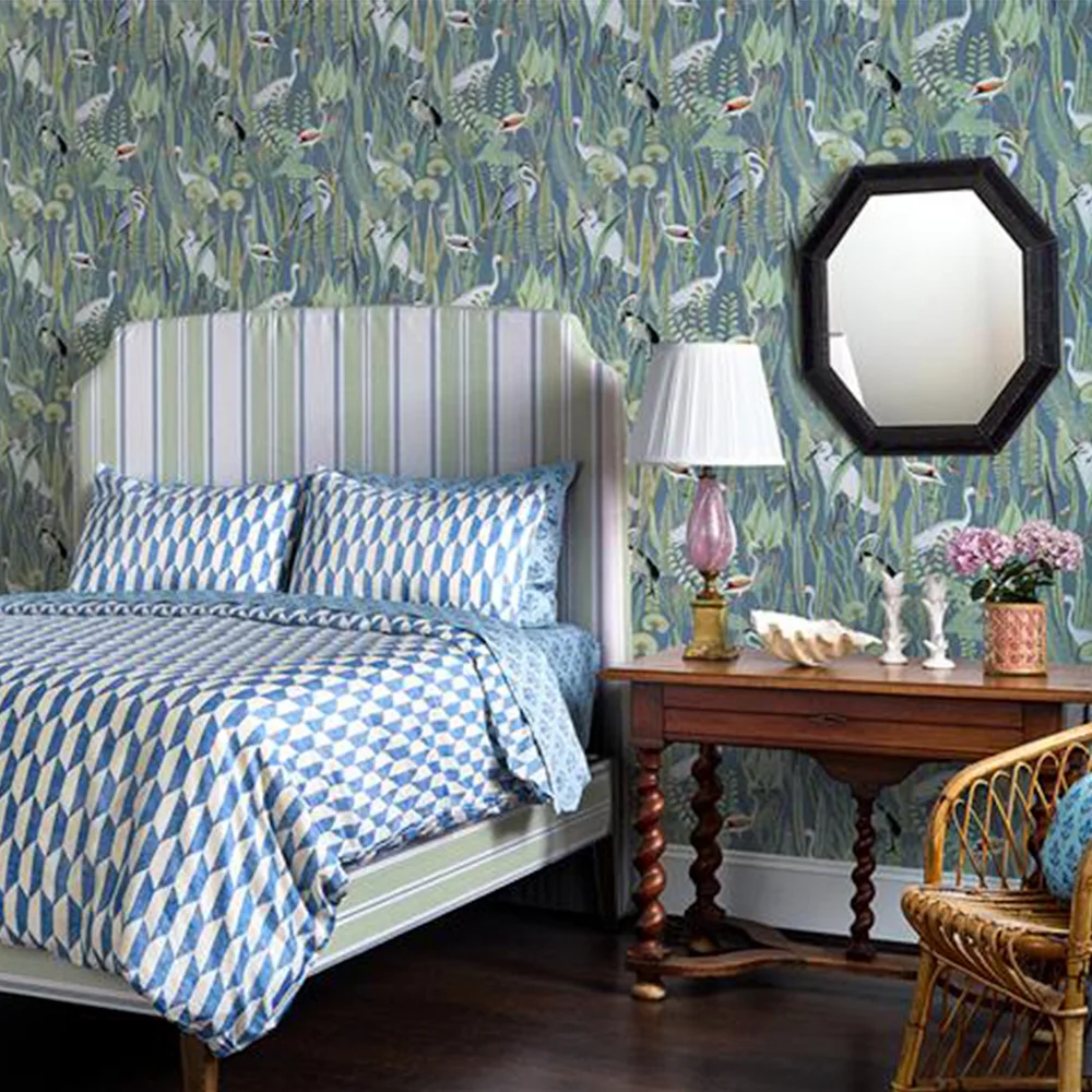 Bedroom with heron wallpaper, blue and white geometric bedding and a headboard upholstered in green stripes fabric.