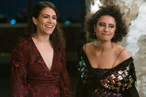 Abbi Jacobson and Ilana Glazer at an event. Abbi wears a V-neck dress with floral patterns, while Ilana wears a sequin dress with a black draped shawl
