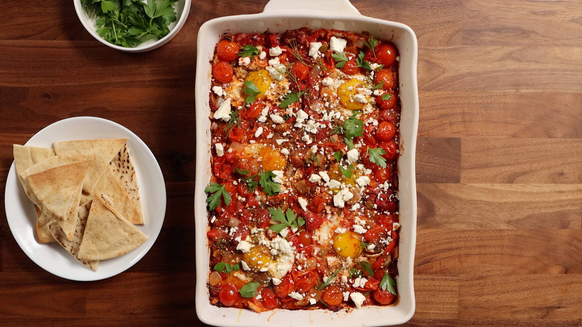 baked shakshuka in a casserole dish with herbs and pita on the side