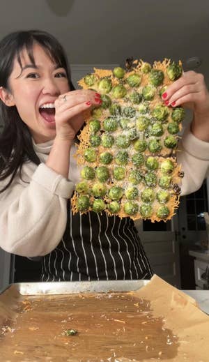 Person holds up a large sheet of baked cheese with Brussels sprouts embedded in the sheet.