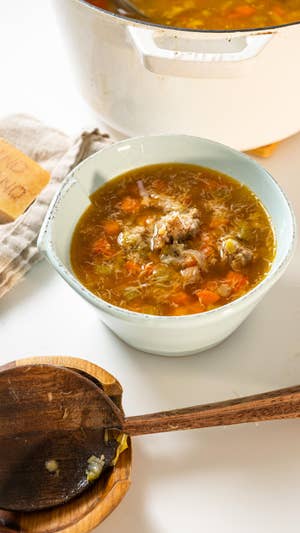 White bowl filled with sausage lentil soup sitting on a table alongside a large wooden spoon in a wooden bowl