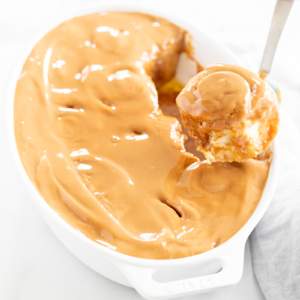 A person scooping cookie butter cinnamon rolls from a white dish.