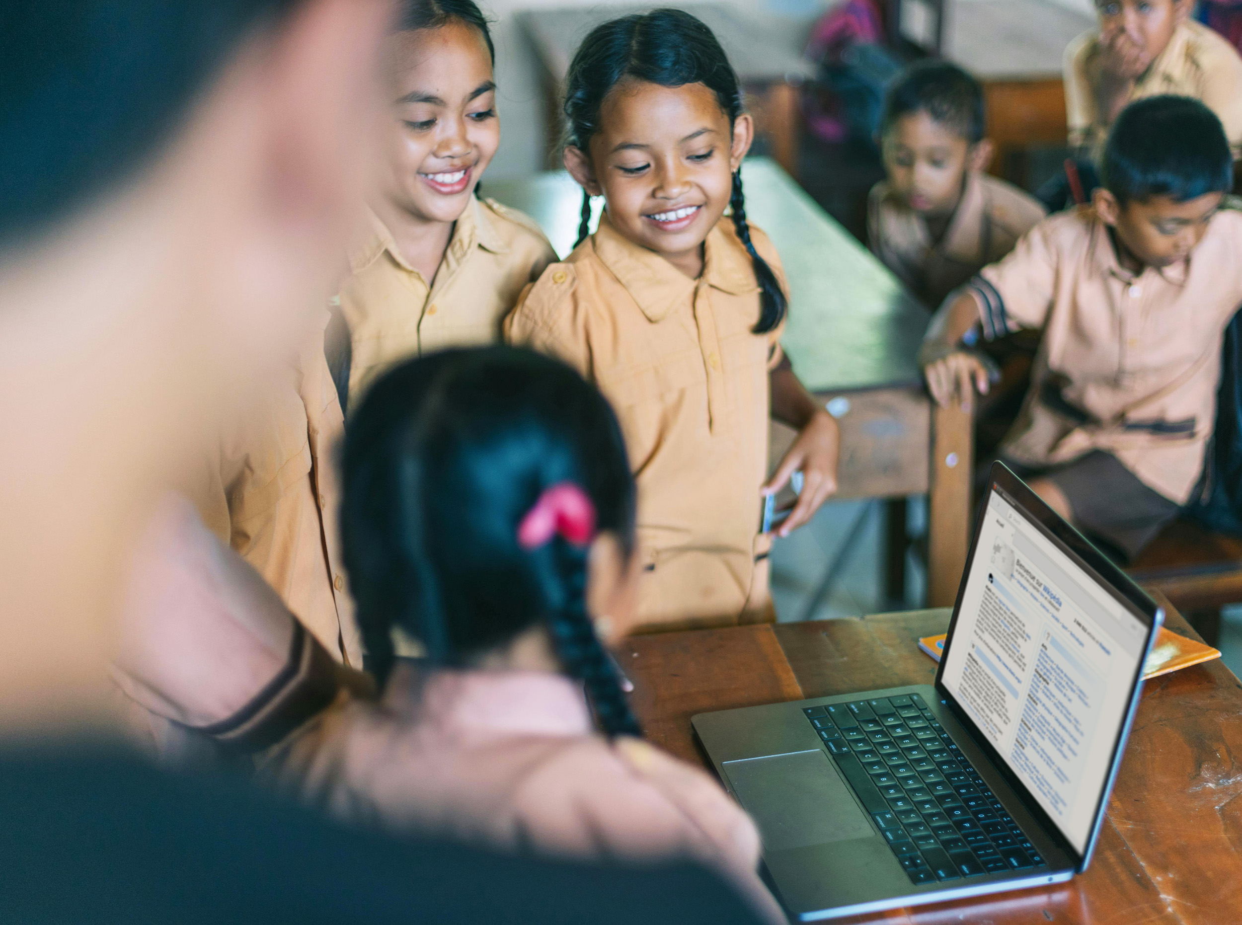 Young children in school uniform gathered around a laptop smiling