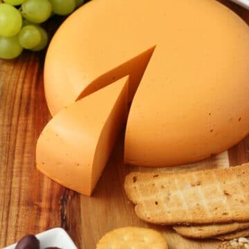 Vegan cheddar cheese on a wooden board with grapes and crackers.