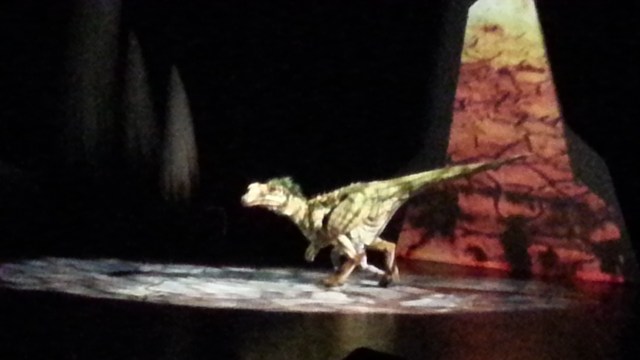 A man in an elaborate dinosaur costume steps into a spotlight