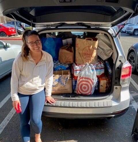 A woman stands next to an open SUV trunk filled with various grocery bags, including Trader Joe's and Target.