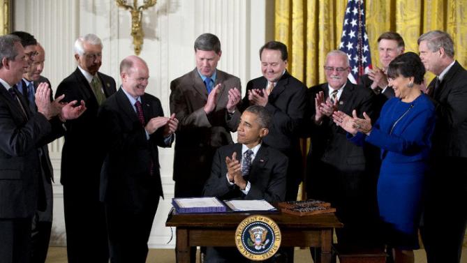Surrounded by Cabinet officials and members of Congress, President Barack Obama applauds after signing H.R. 2146 Defending Public Safety Employees Retirement Act and H.R. 1295 Trade Preferences Extension Act of 2015 , Monday, June 29, 2015, in the East Room of the White House in Washington. From left are, U.S. Trade Representative Michael Froman, Treasury Secretary Jacob Lew, Rep. John Delaney, D- Md., Rep. David Reichert, R-Wash., Sen.. Chris Coons, D-Del., Rep. Ron Kind, D- Wis., Rep. Pat Tiberi, R-Ohio, Rep. Gerald Connolly, D-Va., Rep. Donald Beyer, D-Va., Commerce Secretary Penny Pritzker, and Agriculture Secretary Tom Vilsack. (AP Photo/Carolyn Kaster)