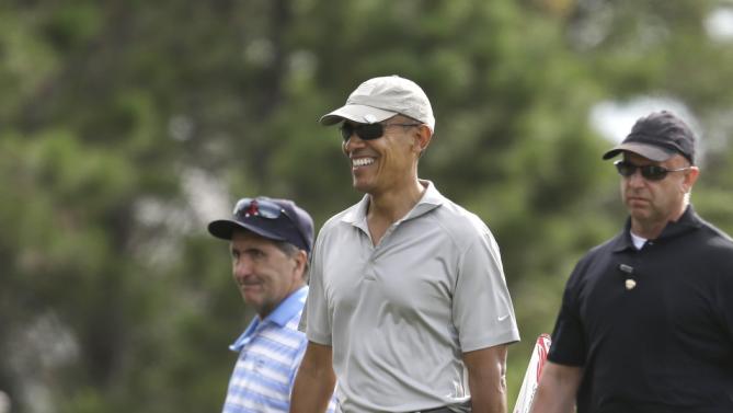 President Barack Obama, center, smiles as he steps off a green after putting while golfing Saturday, Aug. 8, 2015, at Farm Neck Golf Club, in Oak Bluffs, Mass., on the island of Martha's Vineyard. Obama is spending his first full day of vacation on the island playing golf. (AP Photo/Steven Senne)
