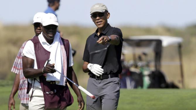 President Barack Obama, center, receives a club from a caddy, front left, while golfing at Vineyard Golf Club, in Edgartown, Mass., on the island of Martha's Vineyard, Monday, Aug. 10, 2015. The president is staying on Martha's Vineyard with first lady Michelle Obama and daughter Sasha for a 17-day island retreat. (AP Photo/Steven Senne)
