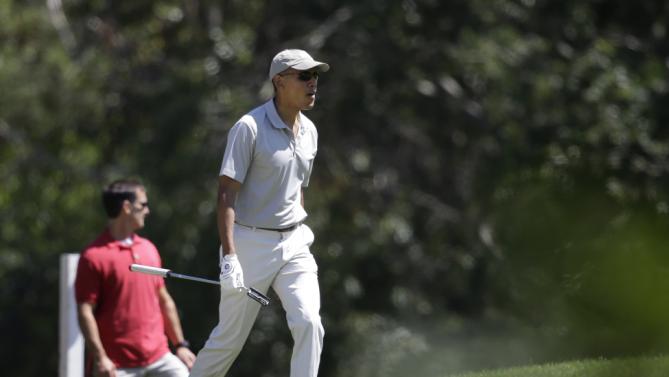President Barack Obama, right, carries a golf club as he approaches a green while golfing Saturday, Aug. 8, 2015, at Farm Neck Golf Club, in Oak Bluffs, Mass., on the island of Martha's Vineyard. Obama is spending his first full day of vacation on the island playing golf. (AP Photo/Steven Senne)