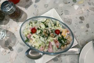 A glass bowl filled with a fresh salad containing shredded lettuce, diced tomatoes, cucumber, and small pieces of croutons.
