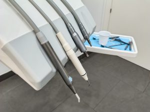 Collection of dental instruments attached to a dental chair. There are three tubes, each with a different tip suggesting they are tools for dental procedures. Below them, there’s a tray containing several dental instruments.