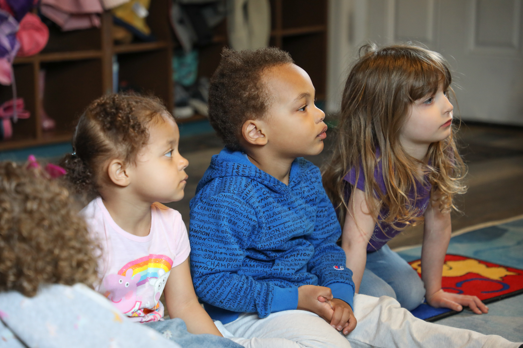 photo of three children seated on a rug and looking ahead during story time at Happy Go Lucky Childcare