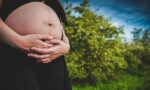 Uma fotografia de perto retrata uma pessoa grávida, com as mãos segurando a barriga, em um ambiente ao ar livre. • SciELO em Perspectiva | Press Releases Uma fotografia de perto retrata uma pessoa grávida, com as mãos segurando a barriga, em um ambiente ao ar livre.