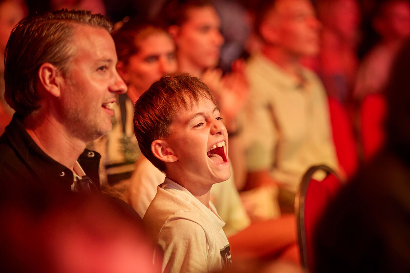 A close-up of a young boy smiling as he watches the Maximum Pro Wrestling show at Butlin's, with his father.