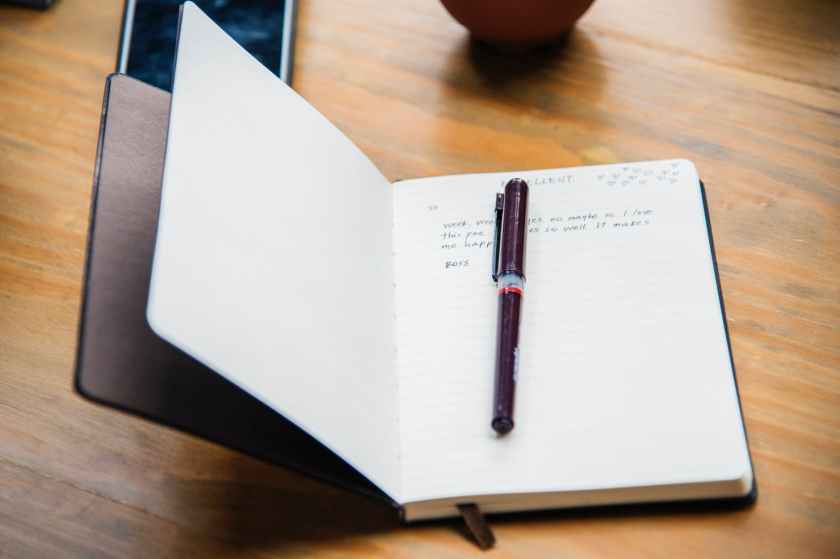 black and blue plastic pen non top of black covered notebook