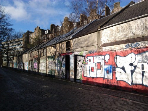 The other side - mews functioning as lockups. In one, the open throat of an old car, being repaired or abandoned