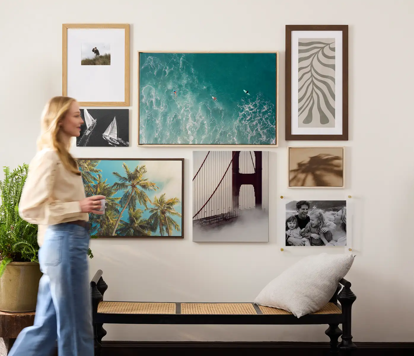 Gallery wall of coastal, nature, and architectural prints above a bench with a plant nearby in a bright, modern room.