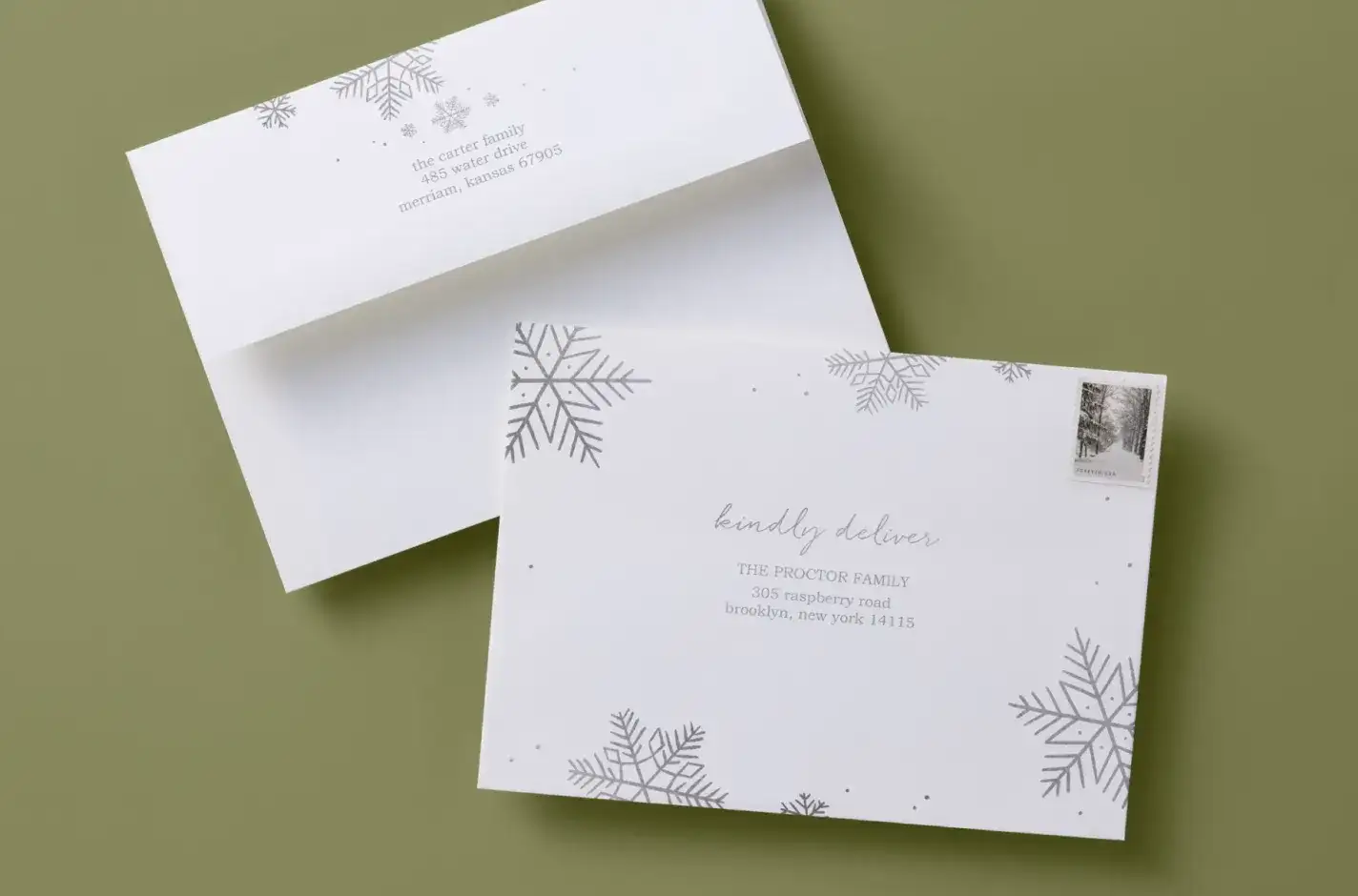 Holiday mailing envelopes with silver snowflake designs and printed return addresses, arranged on an olive background with winter stationery style