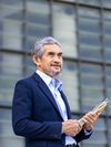A confident, senior Asian business executive stands outdoors against a cityscape while holding files.