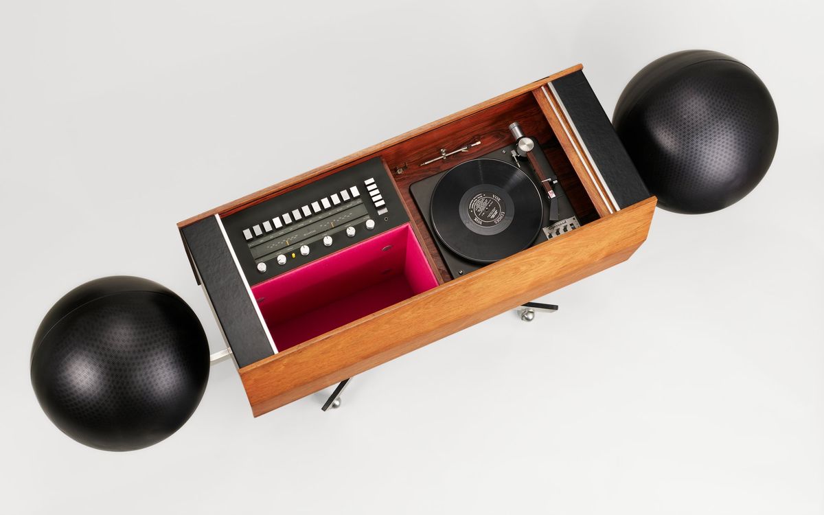 Color photo of a stereo system from above, with two black spheres at either end and a rectangular wood cabinet containing a tuner/ receiver and turntable.