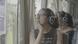 A young woman in a black, sleeveless shirt listen to her headphones while staring out of a bus window A young woman in a black, sleeveless shirt listen to her headphones while staring out of a bus window