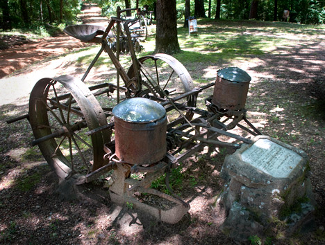 JOE_3363 A large number antique farm implements place around the grounds are visible evidence of the agrarian nature of the areas economy in the 19th and early 20th centuries. Plaques at every piece of equipment give evidence of it use. This horse-drawn planter is a good example. The planter was donated to the cemetery collection in memory of Tate “Uncle Bud” McGehee “Miss Vaughn” McGehee. Family member Edgar Colvin installed the planter at the cemetery, The plaque information, typical of the collection reveals a story. The planter was bought by Mr. McGehee in 1920. He always said, “ ... this planter is so accurate that if it drops two seeds in a hill, it will reach back and pick up one of them.”