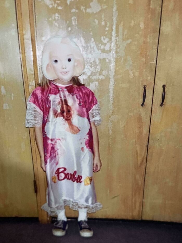 Child wearing a bizarre Barbie dress and a creepy mask, creating a weird and unsettling visual effect indoors. Child wearing a bizarre Barbie dress and a creepy mask, creating a weird and unsettling visual effect indoors.