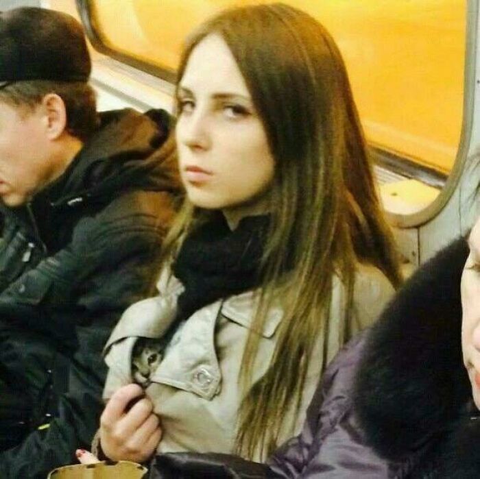 Young woman on public transit with a small cat hidden inside her coat, a picture that goes hard and makes people chuckle. Young woman on public transit with a small cat hidden inside her coat, a picture that goes hard and makes people chuckle.