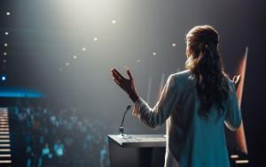Back of a woman standing in front an audience holding both hands up