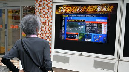 Une femme regarde l'édition spéciale de la télévision publique japonaise NHK, dans le centre de Tokyo, le 30 juillet 2025. (RICHARD BROOKS,RICHARD A. BROOKS / AFP)