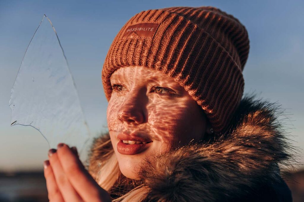A girl is looking at the light's reflections through ice.
