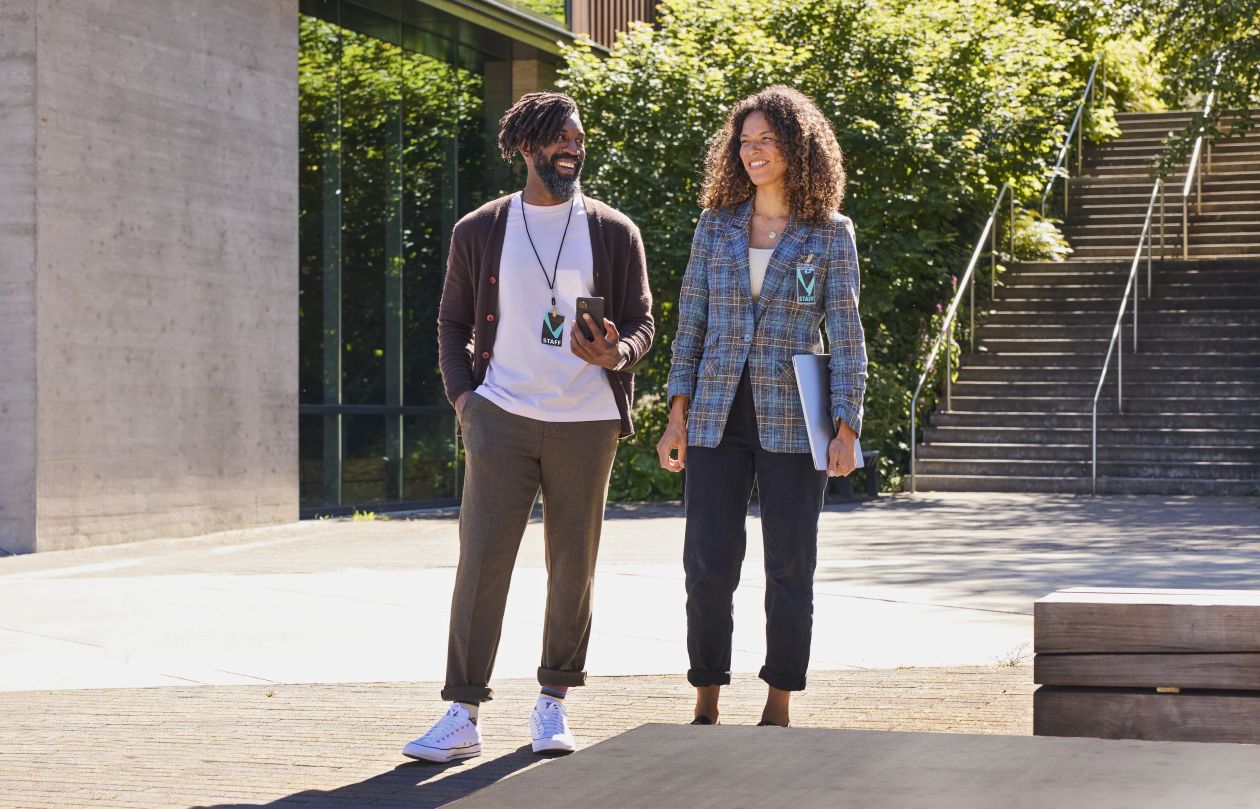 Two higher education leaders walk together outside on a college campus.