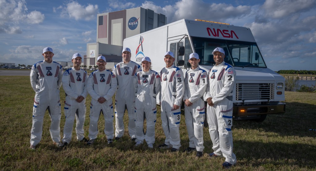 Members of the Artemis II closeout crew, from left, William Sattler; Tyler Sutherland; Michael Heinemann; Christian Warriner; Taylor Hose; Jenni Gibbons, Artemis II backup crew member; Bill Owens; and Andre Douglas, Artemis II backup crew member, pose for a photo with NASA’s Vehicle Assembly Building behind them at the agency’s Kennedy Space Center in Florida on Thursday, Dec. 19, 2025. The closeout crew is responsible for safely securing the astronauts inside the Orion spacecraft on launch day and closing the hatch during launch countdown.